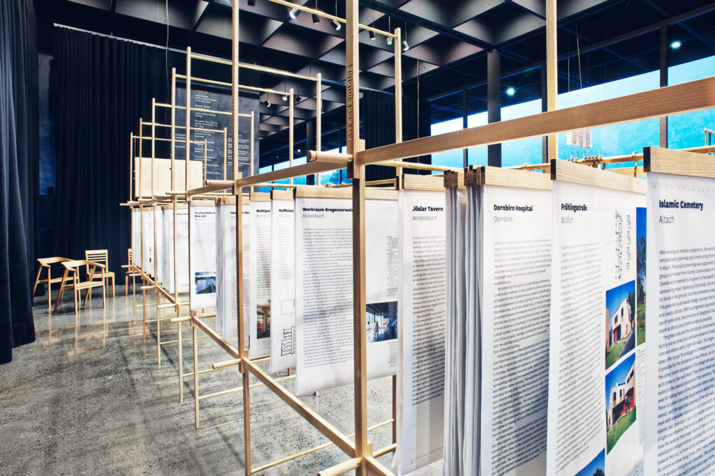 Exhibition View Werkraum: Mehrere große, hängende Informationsplakate in einem modernen, hellen Ausstellungsraum mit Holz- und Metallrahmen.